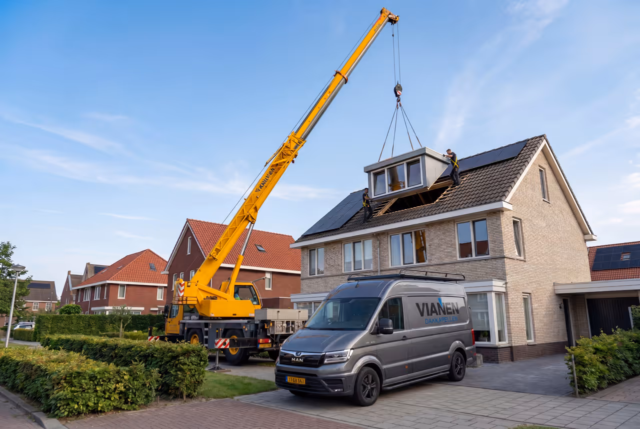 Kraan plaatst dakkapel op een huis met twee medewerkers op het dak naast een bus van Vianen Dakkapellen.